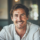 Homme souriant en chemise blanche, intérieur lumineux.
