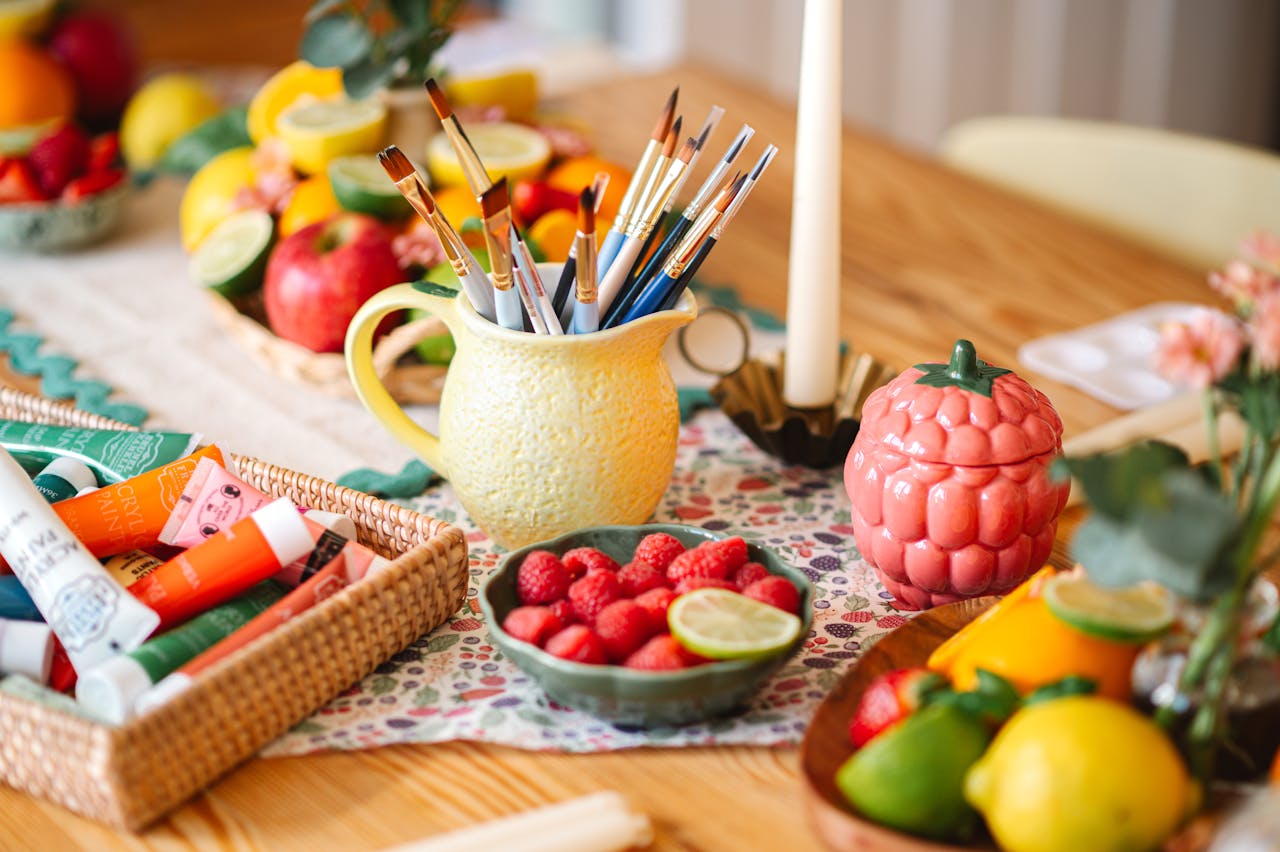 Colorful still life of art supplies, fruits, and paints on a wooden table, ideal for creative projects.