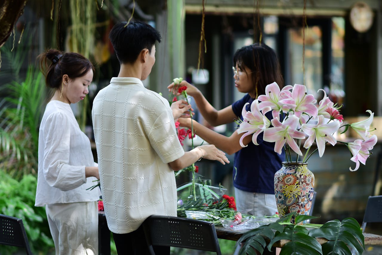 our-story Three people engaged in floral arrangement in a vibrant garden setting, focusing on lilies.