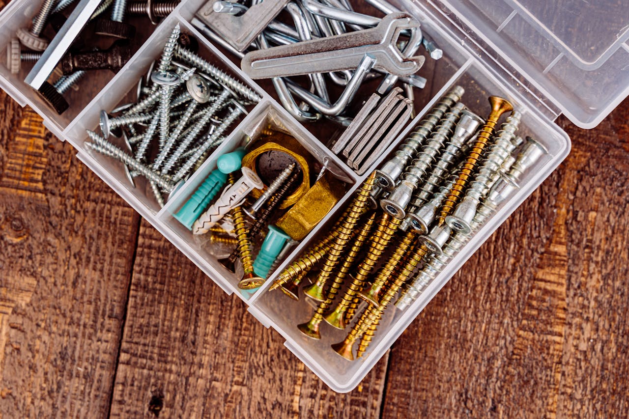 Top view of assorted screws and tools in a plastic organizer on wooden surface.